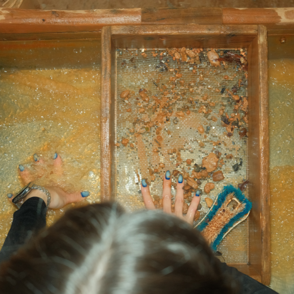 Person sorting through small rocks or stones on a筛 (sieve) with a wooden frame.